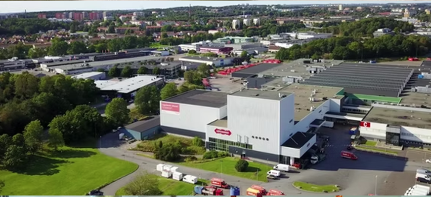 Flygfoto över ett industriområde med Göteborgs nya bryggeri i förgrunden, omgiven av lastbilar, grönområden och fler industribyggnader i bakgrunden.