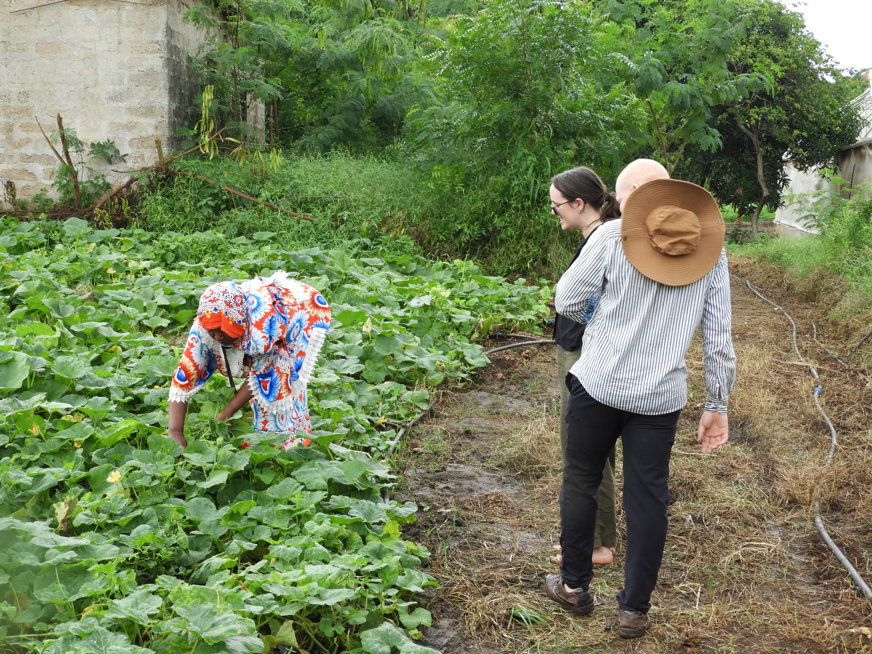Tre personer besöker ett plantage utanför Dar es Salaam. En person gräver i ett land och de andra två kollar på. En av dem har albinism.