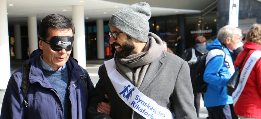 Man från synskadades riksförbund ledsagar man med ögonbindel