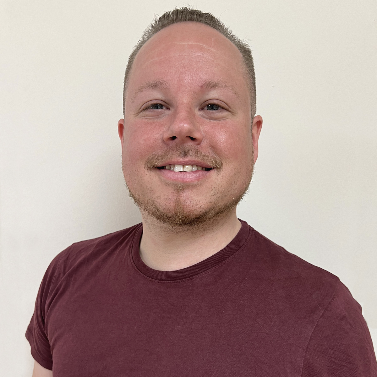 Leende man i 30-årsåldern. Kort hår, snaggat på sidorna. Vinröd t-shirt.
