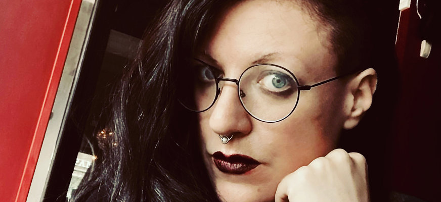 Anna Wallsten lutar ansiktet mot sin knutna näve. Hon har mörkt hår, bär runda glasögon och har mörkrött läppstift.