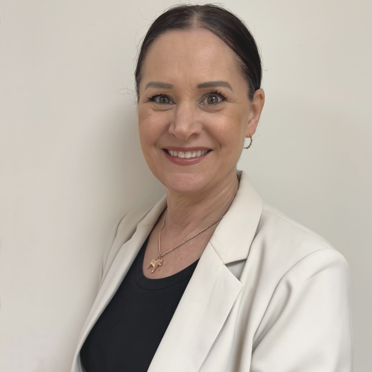 Leende kvinna i 50-årsåldern i hästsvans, vit kavaj.