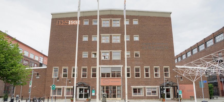 Framsidan av Esters Restaurang vid Ester Mosessons Gymnasium i Göteborg, med tegelbyggnad, flaggstänger och entré