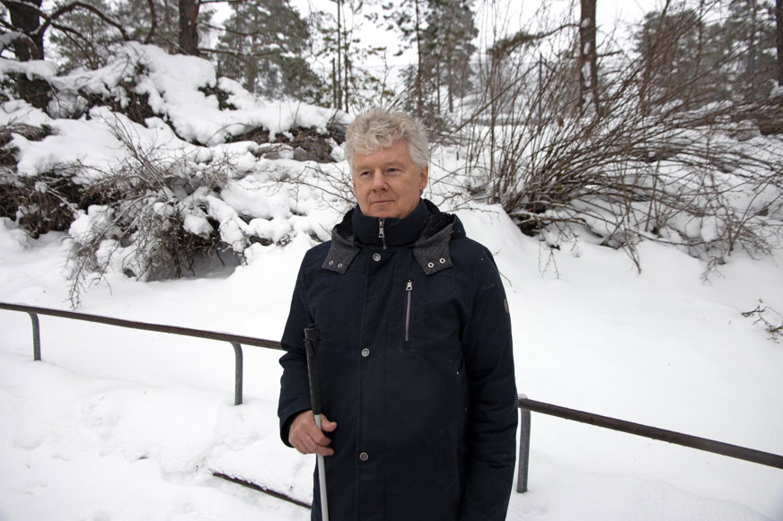 Niklas Mattsson i vinterlandskap. Han är klädd i mörkblå jacka och står med sin vita käpp i handen. Blicken är fäst utanför bild och han har ett tänkande ansiktsuttryck.