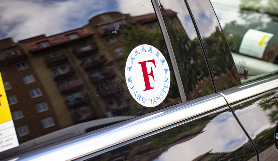 Bild på svart färdtjänstbil. På rutan sitter ett klistermärke med färdtjänstens logotyp i Stockholm.