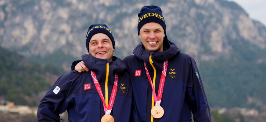 Zebastian Modin och guiden Emil Talsi har på sig blågula träningskläder och mössor. Bronsmedaljer hänger runt deras halsar. De håller om varandra, ler stort och i bakgrunden syns ett berg.