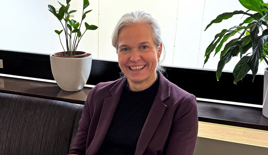 Jenny Ögren sitter i en soffa på SRF:s Rikskansli. Hon har grått, uppsatt hår och en lila kavaj över en svart tröja. Hon ler stort mot kameran.