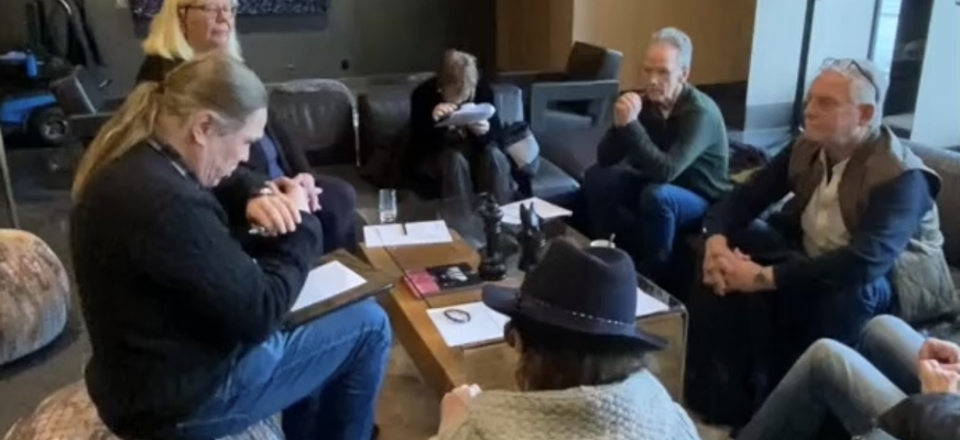 En grupp personer sitter samlade runt ett bord i en lounge-liknande miljö och deltar i en utbildningsdiskussion under en aktivitetsledarutbildning.