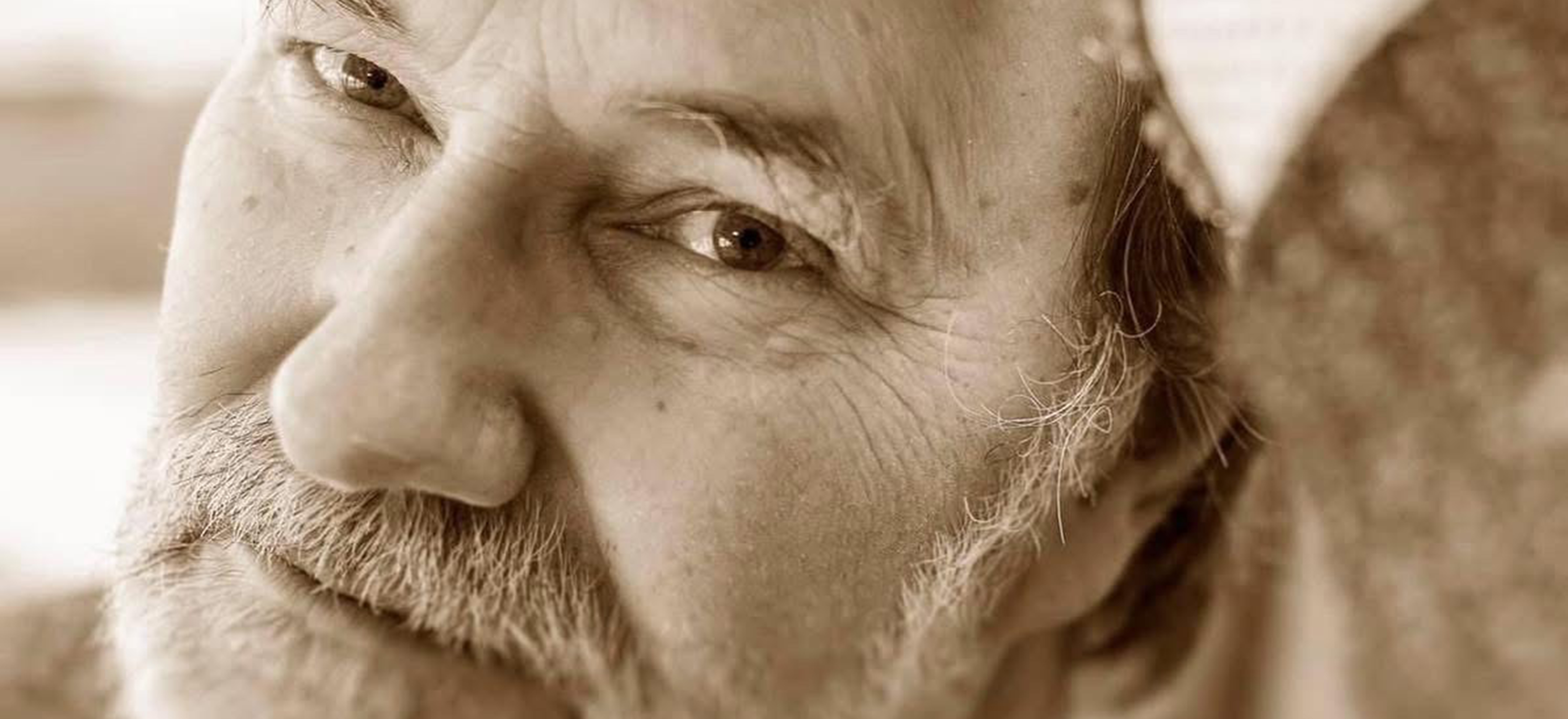 Svartvit porträttbild på Micce Rylander med gult filter. Micce har grått, kortklippt skägg. Han stödjer sitt huvud i händerna och kollar rakt in i kameran.