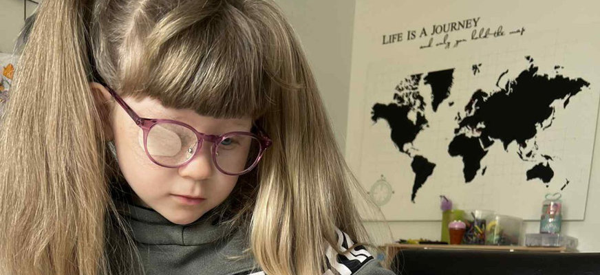 Wilja har håret uppsatt i två tofsar på sidorna och bär stora glasögon. I bakgrunden syns en världskarta uppsatt väggen med orden ”Life is a journey” ovanför.