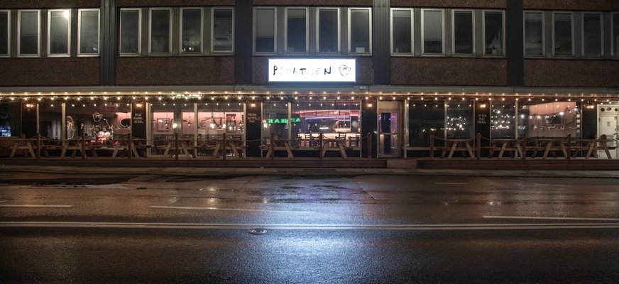 Bilden visar utsidan på restaurang potatisen på kvällen. Mans er restaurangens skylt med loggan som lyser ovanför entrén