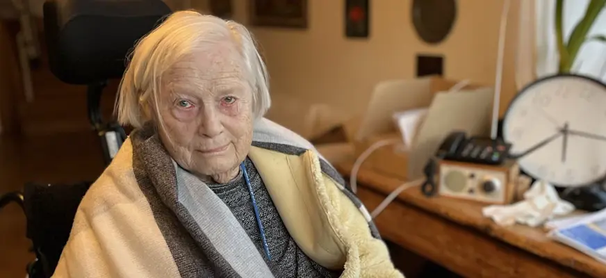 Kerstin Hansson sitter i en rullstol i sitt hem med överkroppen insvept i en filt.