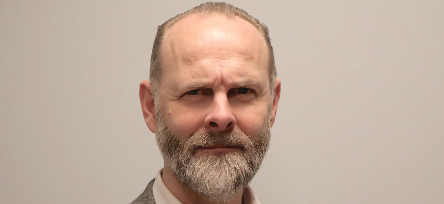 Klas Nelfelt, ordförande i Förbundet Sveriges Dövblinda, tittar in i kameran med allvarlig min. Han har grått skägg och bär kavaj med en ljus skjorta under.