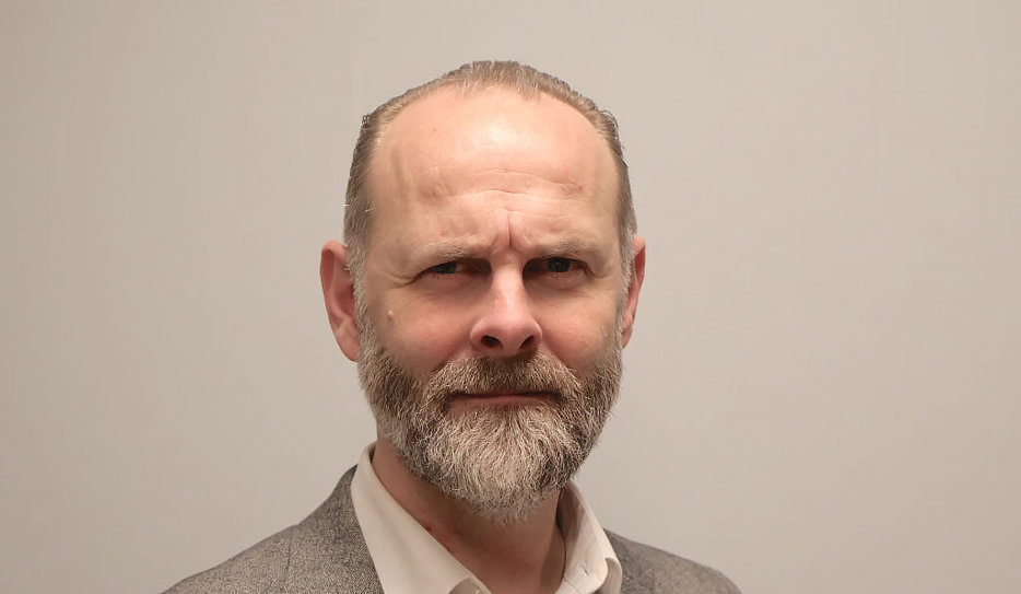 Klas Nelfelt, ordförande i Förbundet Sveriges Dövblinda, tittar in i kameran med allvarlig min. Han har grått skägg och bär kavaj med en ljus skjorta under.