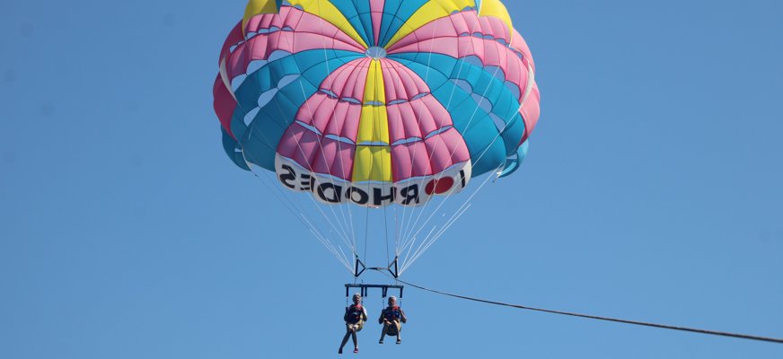 Två personer glidflyger på långt avstånd mot klarblå himmel.
