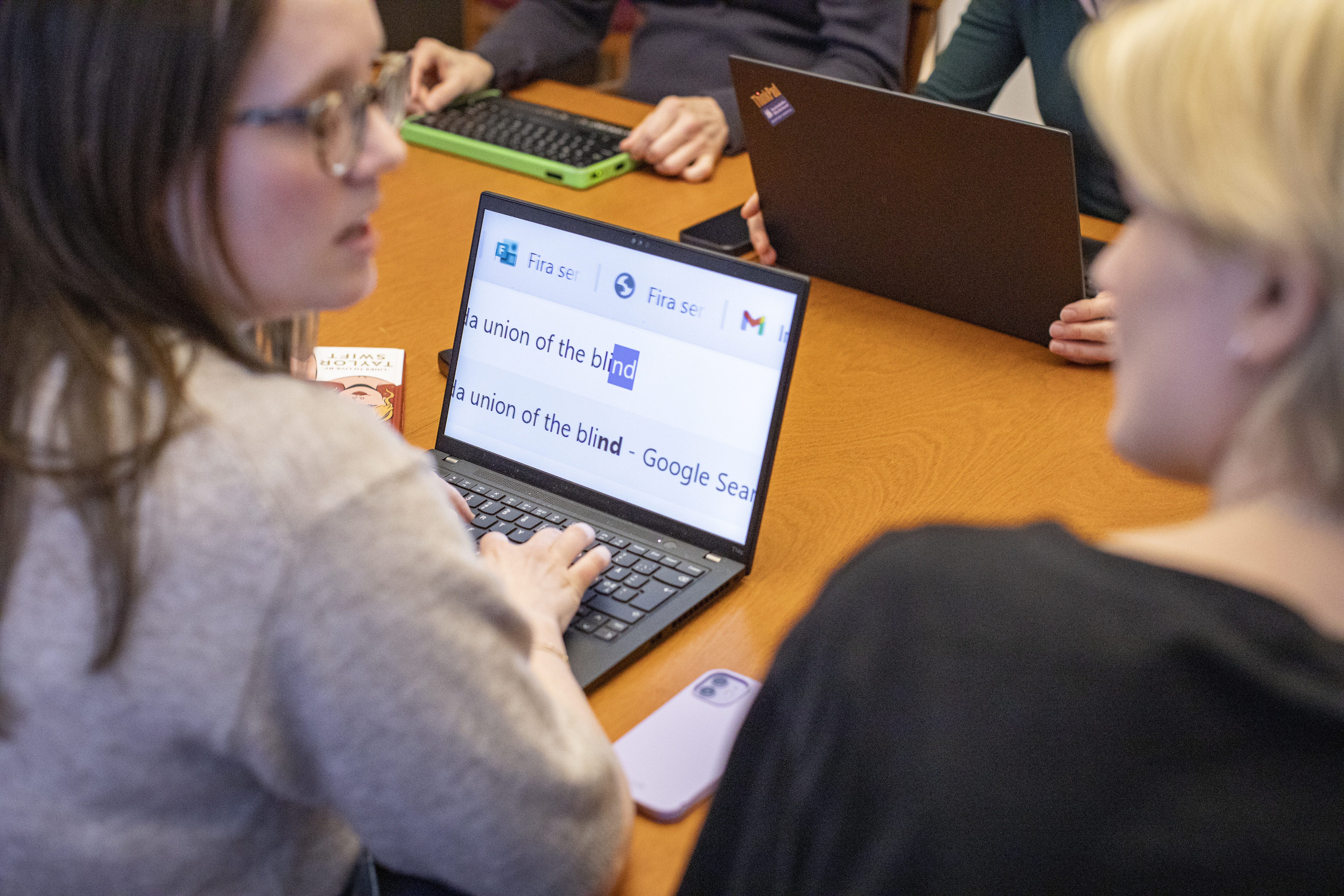 En grupp personer sitter i ett konferensrum. Två personer i förgrunden diskuterar något över en dataskärm med förstoring.