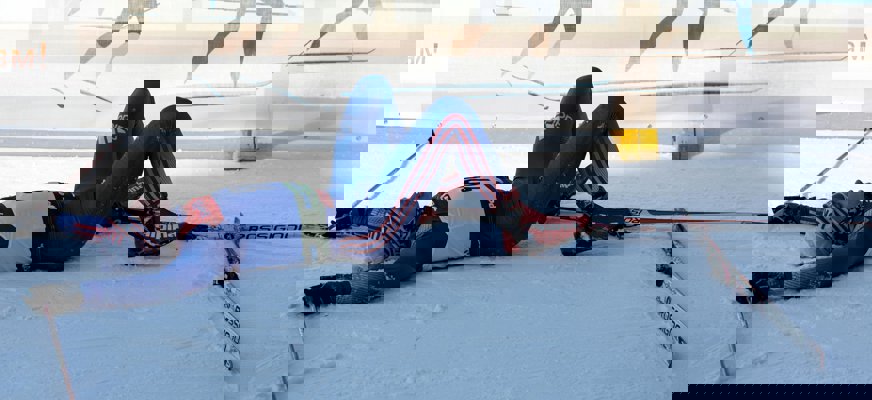 En längdskidåkare ligger på rygg efter avslutat lopp och andas ut.