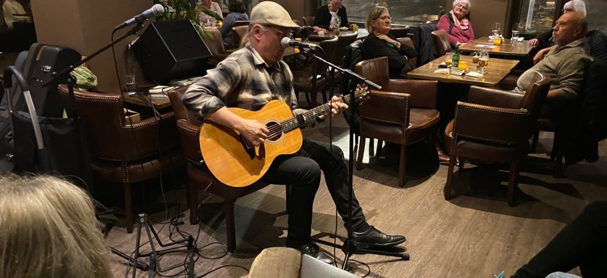 En bild på State Lykke som sitter och spelar gitarr och sjunger i en Café miljö