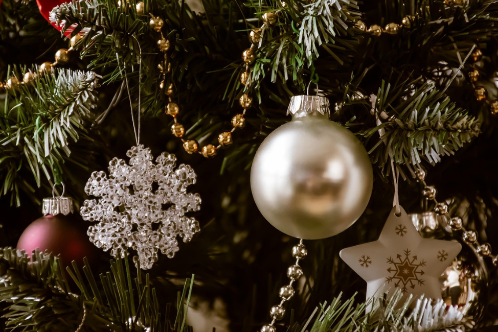 En närbild av en julgran med julgranskulor och pynt, bland annat en glittrande snöflinga, en guldig kula och ett guldigt snöflingehänge