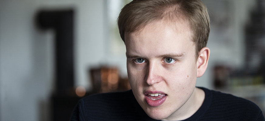Porträttbild av Anton Nilsson. Han har mörkblont kort hår och har på sig en svart finstickad tröja med rund krage.