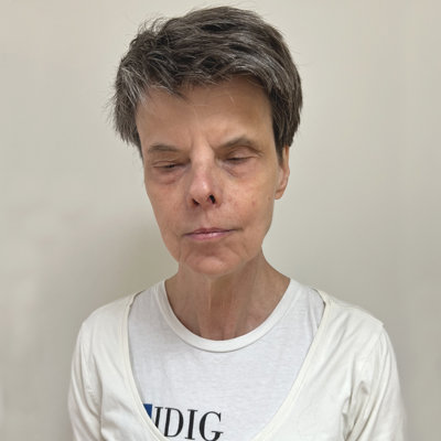 Kvinna i 60-årsåldern, kort mörkgrått hår, vit t-shirt.