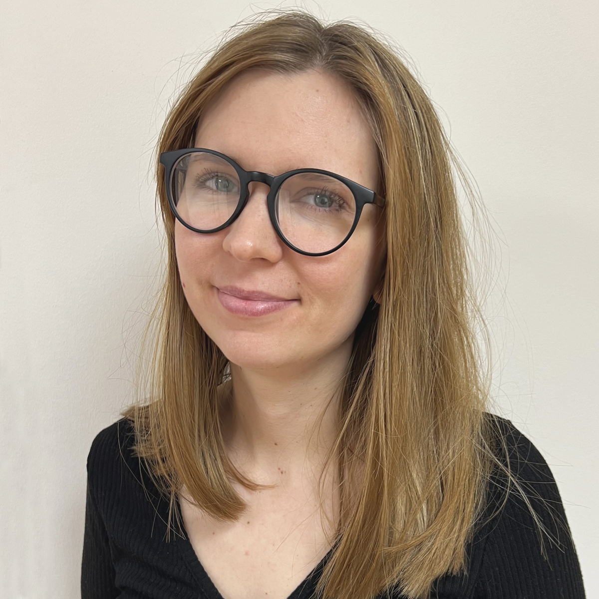 Leende kvinna i 30-årsåldern, mörka glasögon, långt rågblont hår, svart v-ringad tröja.