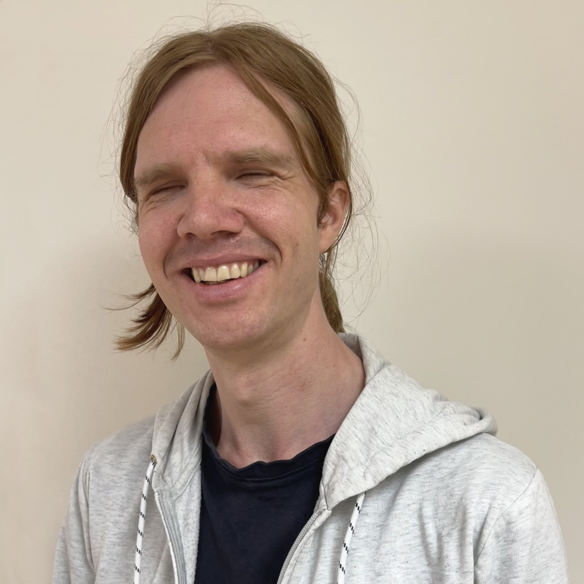 Leende man i 30-årsåldern, uppsatt långt rödbrunt hår, grå munkjacka, svart t-shirt.