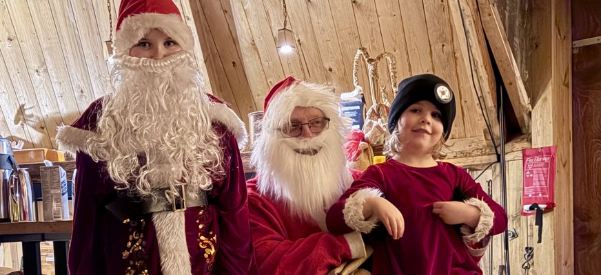 En tomte och två tomtenissar med röda dräkter. Tomten och den ena nissen har röda luvor och vita skägg. Den andra tomtenissen saknar skägg och har en svart mössa på sig. 