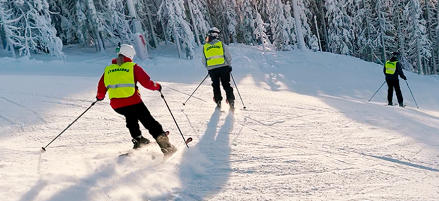 Tre personer i varselväst åker skidor