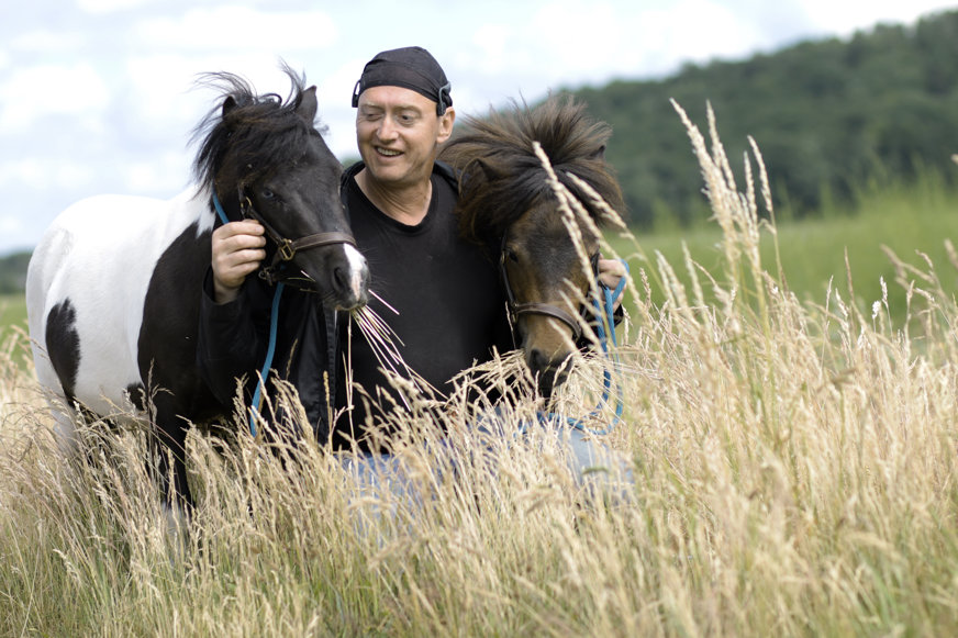 Jan står på en äng med en häst på var sin sida om honom.