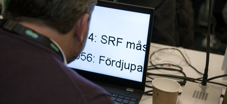 Man fotad bakifrån försjunken i sin laptop med stor förstoring, orden "SRF mås-" och "Fördjupa" syns.