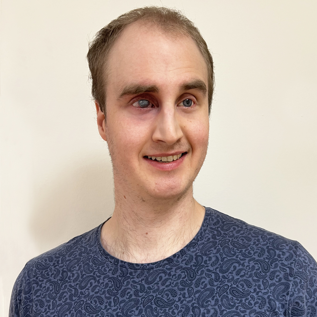 Porträttbild man i 30-årsåldern, kort brunt hår, paisleymönstrad blå t-shirt.