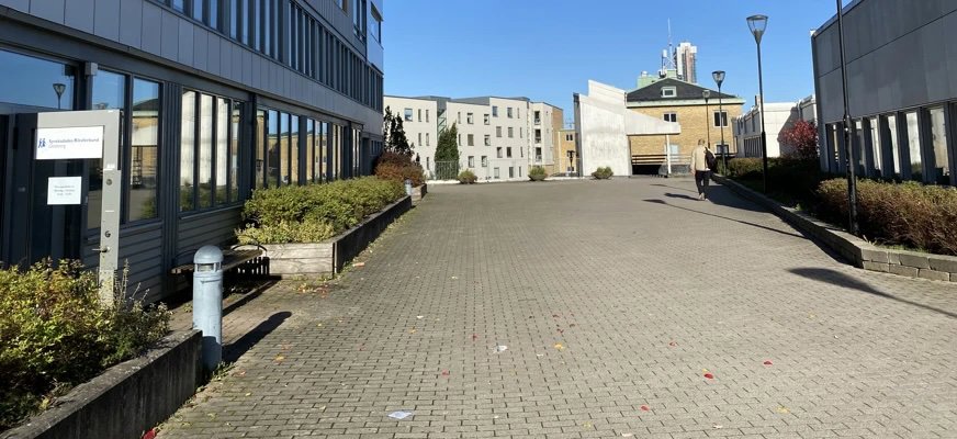 Bilden är tagen utanför Masthuggsterrassen 4. Det är stora hus och blå himmel med lite grönt längs fasaden.