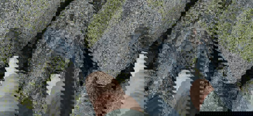 Fötter i vandringsskor som går mellan mossiga stenar.