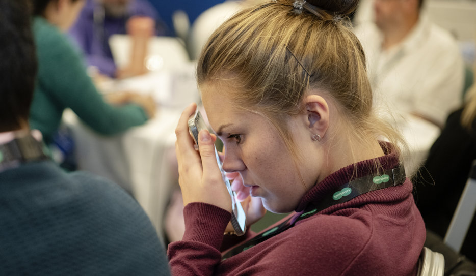 Kvinna med uppsatt hår försjunken i smartphone som hon håller tätt mot ansiktet