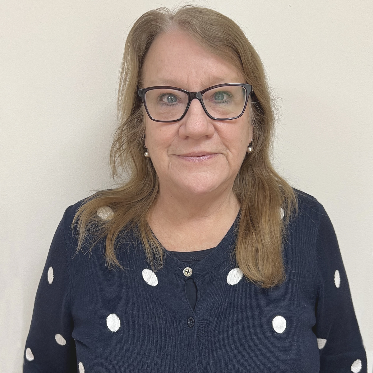 Kvinna i 60-årsåldern med långt brunt hår, mörka glasögon, prickig kofta.