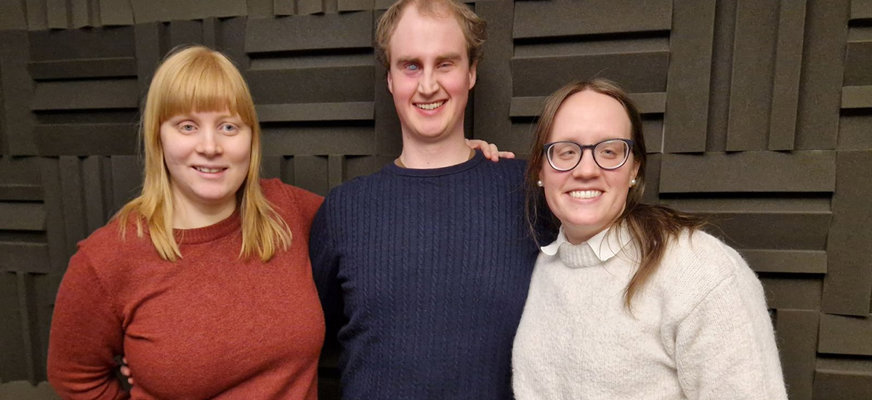 På bilden står Sofie, Linus och Erika tillsammans framför en vägg med mörka ljudabsorberande paneler, alla tre ler glatt mot kameran.