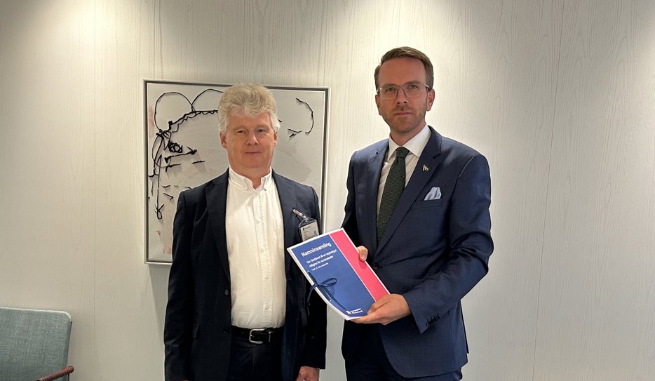 Niklas Mattsson lämnar över namninsamlingen till Andreas Carlson. Båda männen har mörka kavajer och vit skjorta och befinner sig i ett mötesrum på regeringskansliet. Bakom dem skymtar en tavla med ett svartvitt mönster.