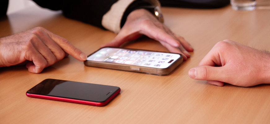 Två personer sitter mittemot varandra vid ett bord och tittar på en mobiltelefon.
