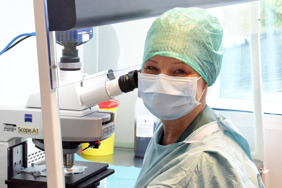 En kvinna i laboratorium iförd mask, skyddskläder och hårskydd.