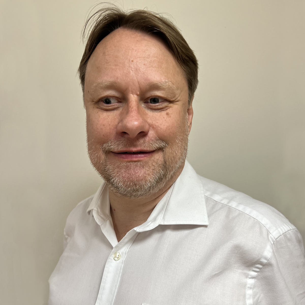 Man i 40-årsåldern, grå skäggstubb, vit skjorta, brunt hår.
