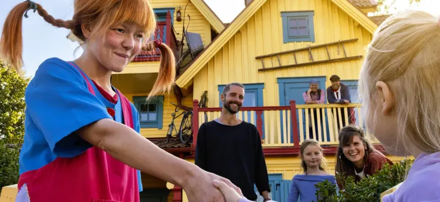 Pippi Långstrump skakar hand med ett barn framför Villa VIllekulla
