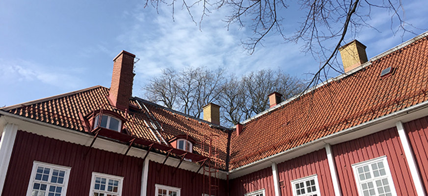 Bilden visar en stor röd trävilla med vita knutar i vinkel