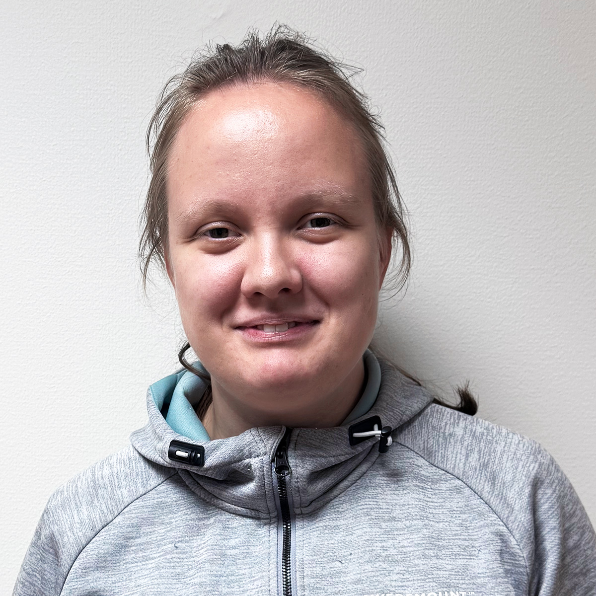 Porträttbild av Sofia, en kvinna i 20-årsåldern med brunt uppsatt hår och bruna smala ögon. Hon är klädd i grå hoodie med blått foder. Hon ler mot kameran.