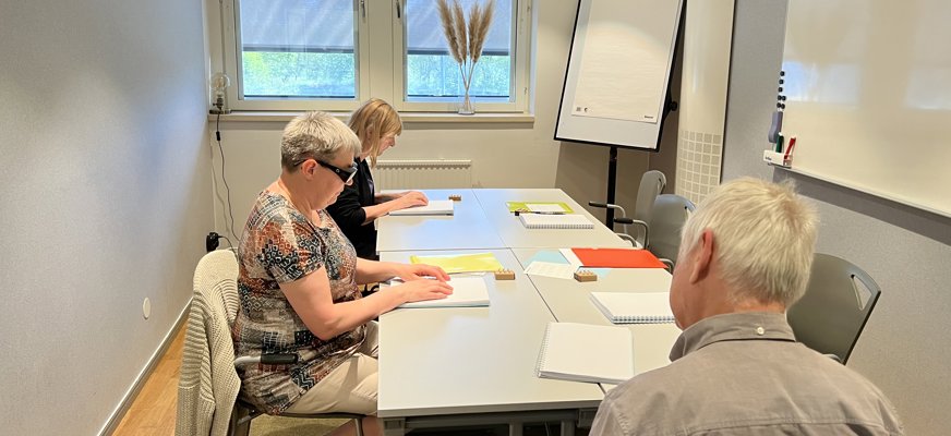 Tre personer vid bord med punktskrift framför sig