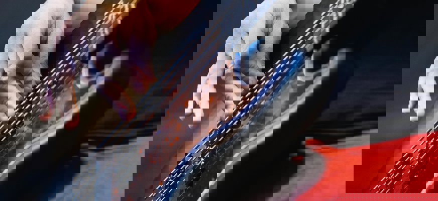 Närbild på en person som spelar elbas. Basen och en hand som spelar är i fokus.