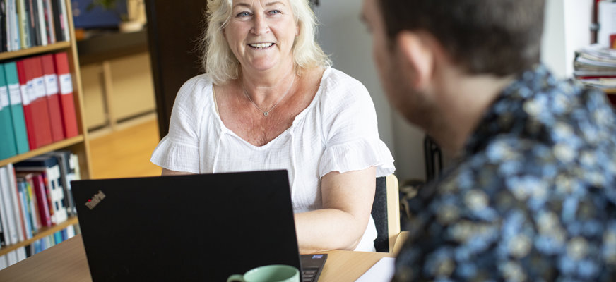 Kvinna vid dator tittar leende mot person mittemot
