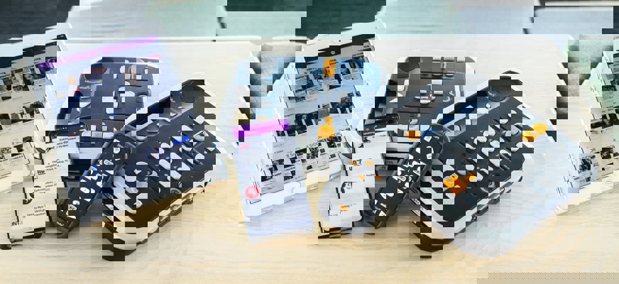 Daisyspelarna Victor Reader Stratus 4, Victor Reader Stratus 12 och Victor Reader Stream ligger på ett bord tillsammans med en läsplatta som visar appen Akila och en mobil som visar taltidningar i appen Legimus.