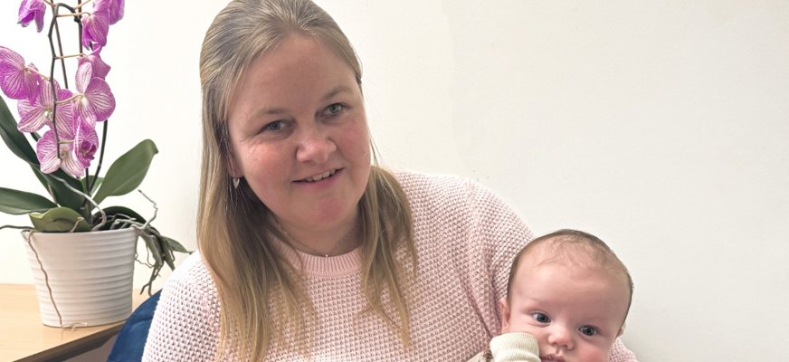 Josefin har rosa tröja och blont hår. Hon håller i en liten bebis med pigg blick och lite brunt hår på huvudet.