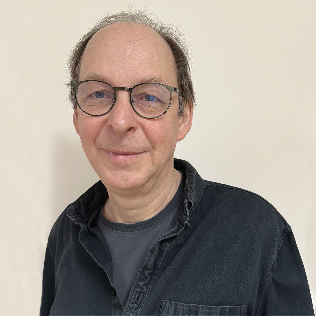 Man i 60-årsåldern, glest brunt hår, rundade glasögon, gråsvart skjorta med t-shirt under.